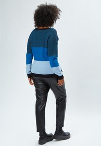 Maglione a strisce blu e nere con vestibilità ampia, polsini a costine e scollo tondo, abbinato a pantaloni in ecopelle neri e stivali con plateau.