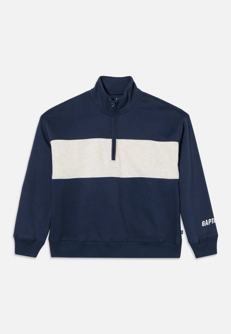 Pull bleu marine avec une bande horizontale blanche sur la poitrine, une fermeture éclair quart de longueur, et le logo GAP sur le poignet de la manche gauche.