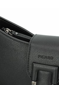 Schwarzlederne Handtasche mit strukturierter Oberfläche, ausgestattet mit einem Reißverschluss und einem ausgeprägten Markenlogo, das auf der Oberfläche geprägt ist. Silberne Hardware-Akzente.