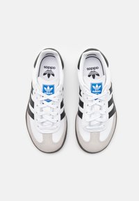 White and gray sneakers with black stripes, leather and suede materials, round toe, lace-up closure, and blue logo on the tongue.