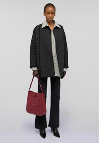 Kvadratmönstrad svart kappa med stora knappar över en randig skjorta, matchad med mörka utsvängda byxor. Vinröd handväska och svarta spetsiga stövlar.