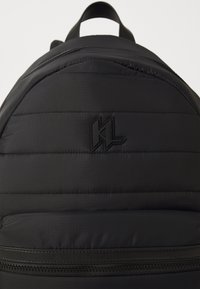 Sac à dos rembourré noir avec un tissu texturé, un logo en relief et une poche frontale zippée pour plus de fonctionnalité.