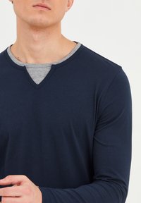 Marineblå langærmet skjorte med V-hals design. Lagt over en grå indre krave. Blød tekstur, letvægtsstof, tætsiddende pasform.