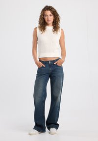White knitted sleeveless crop top paired with loose-fitting dark blue jeans and white sneakers. The top features a textured pattern.