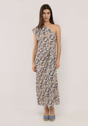 Mujer de pie vistiendo un vestido largo de un solo hombro con un estampado de cachemira multicolor y zapatos de tacón azul.