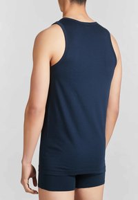 Top in cotone blu navy con scollatura rotonda e ampie aperture per le braccia, abbinato a pantaloni corti aderenti coordinati, visto da dietro.