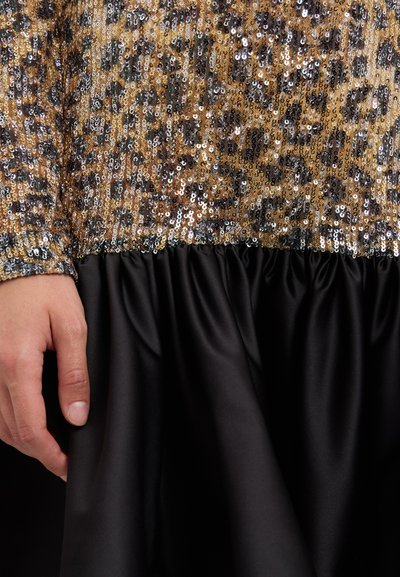 Gespiegelde jurk met een panterprint ontwerp in goud, bruin en zilver aan de bovenkant, overgaand in een zwarte satijnen rok met ruches.