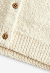 Tessuto a maglia color crema con finitura testurizzata, caratterizzato da una fila di coste e un bottone in legno decorato con un motivo floreale.