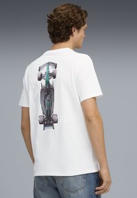 Weißes Baumwoll-T-Shirt mit einem Grafikmotiv eines grün-schwarzen Rennwagens auf der Rückseite. Der Text enthält "2025" und "Aston Martin" in hellgrauer Schrift.