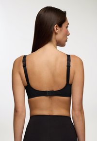 Reggiseno nero senza cuciture con spalline regolabili, chiusura semplice con gancio e tessuto liscio. Progettato per il comfort e per essere poco visibile sotto i vestiti.