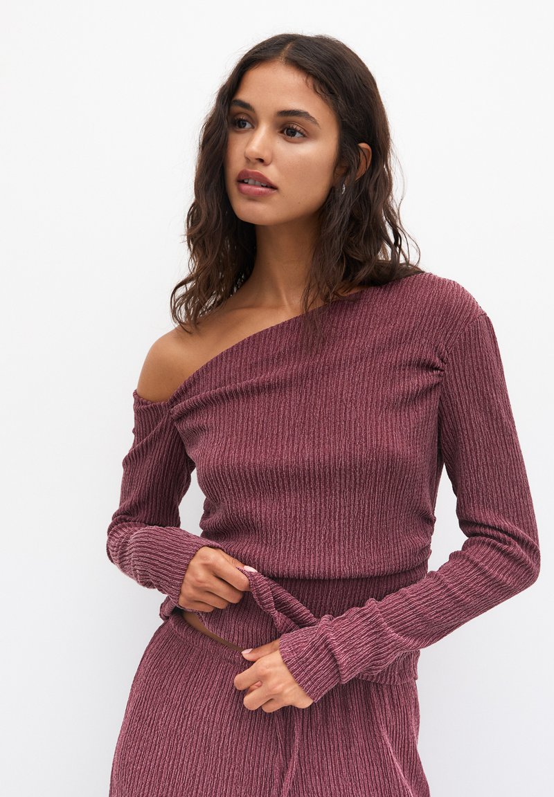 Top a spalle scoperte in maglia di un profondo bordeaux. Maniche lunghe, design aderente e tessuto testurizzato con leggero elastico. Abbinato a pantaloni coordinati.