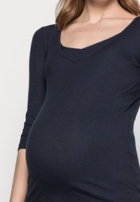 Marineblaues, geripptes Langarmtop mit V-Ausschnitt, dehnbarem Stoff und passender Form für schwangere Figuren.