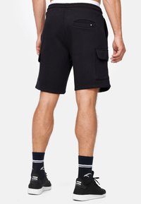 Shorts cargo en coton noir avec une finition texturée, taille élastique et deux poches latérales. Stylés avec des baskets noires et des chaussettes.