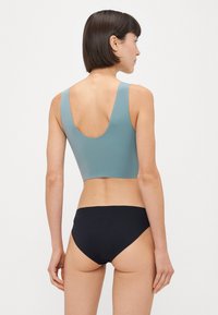 Sportsbh i lys blå, med scoop ryg og brede stropper, parret med sorte bikiniunderdele; glat stof og enkelt design.