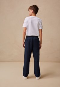 Fehér pamut póló és tengerészkék lenvászon nadrág, laza szabás, rugalmas derékpánttal és oldalzsebekkel, fehér sportcipővel párosítva, semleges háttér.