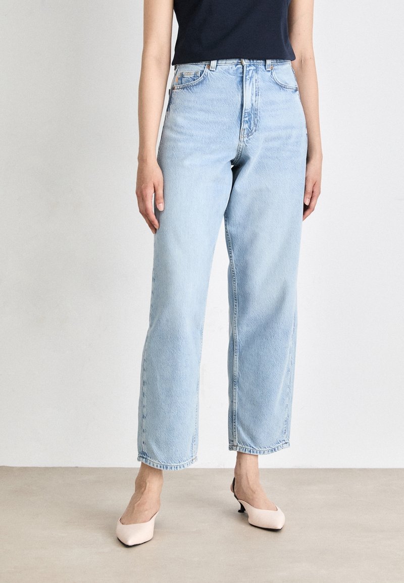 Jasnoniebieskie spodnie typu high-waisted z luźnym krojem, wyróżniające się pięciomasztowymi kieszeniami i delikatnym wyblaknięciem. Połączone z beżowymi szpilkami o spiczastym nosku.