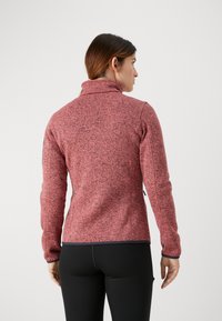 Fleece takki marled punaisesta kankaasta, korkealla kauluksella, pitkät hihat, istuva muotoilu ja kontrastivärinen musta reuna helmassa ja hihoissa.