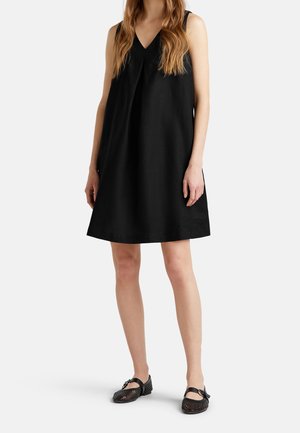 Zwarte mouwloze jurk met een V-hals ontwerp, met een losse pasvorm en een gladde textuur. Gecombineerd met zwart geblokte schoenen en een gespaccent.