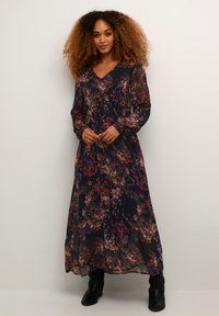 Maxi dress in sheer black fabric with floral patterns in red, pink, and purple. Features a V-neck and long, billowy sleeves. Black ankle boots.