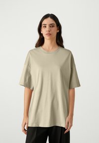 Licht olijfgroene oversized t-shirt met korte mouwen, ronde halslijn en zachte katoen. Eenvoudig ontwerp, geen patronen of accenten.