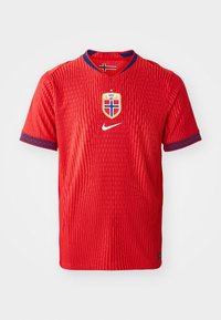 Rød Nike-trøje med struktureret mønster, der har en rund hals, blå detaljer på ærmerne og det norske landslagsmærke på brystet.