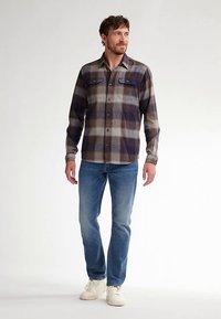 Chemise à carreaux pour homme aux tons bleu marine et beige, confectionnée dans un tissu à la texture douce, dotée de poches à boutons et d'un col classique, associée à un jean bleu.