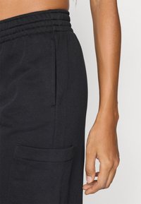 Μαύρο παντελόνι φόρμας με ριμπ ελαστική μέση, πλαϊνή τσέπη cargo και απαλή υφή. Ορατή ραφή στη λεπτομέρεια της τσέπης.