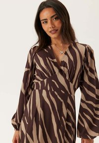 Šaty s dlouhým rukávem s hnědým a béžovým zebřím vzorem, hlubokým výstřihem do V, se sešitým živůtkem a měkkou texturou látky.