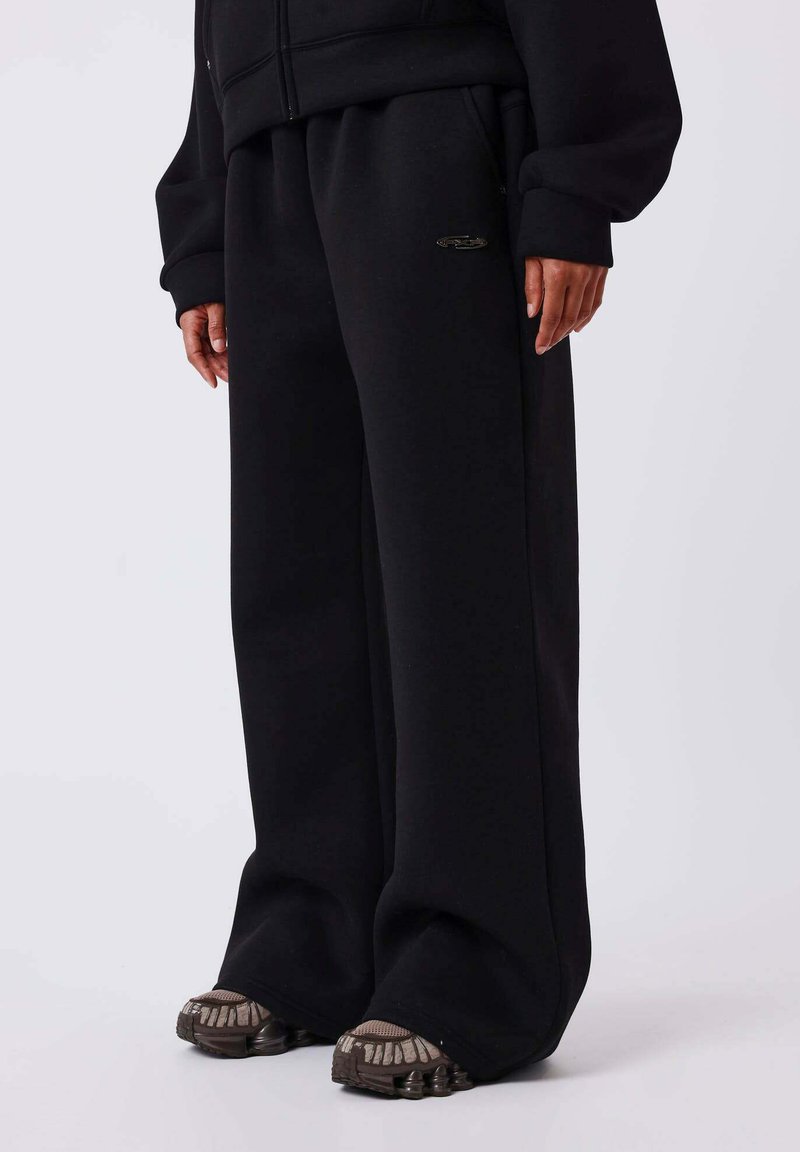 Zwarte oversized joggingbroek gemaakt van zachte, dikke stof met een wijde pijp, voorzien van een elastische tailleband en minimalistische logodetail.
