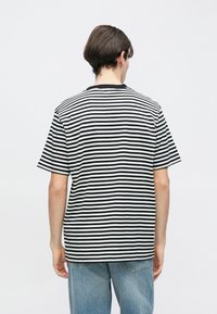 Μαύρο και άσπρο ριγέ μπλουζάκι με κοντά μανίκια και στρογγυλή λαιμόκοψη, φαινομενο από πίσω, συνδυασμένο με ανοιχτό μπλε τζιν.