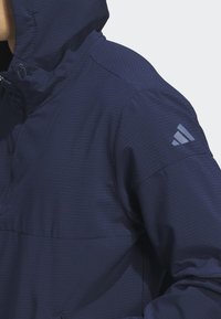 Granatowa bluza z kapturem o strukturalnej fakturze, z frontową kieszenią i odblaskowym logo na lewym rękawie.