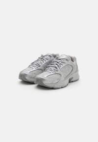 Scarpe da ginnastica argento con un design moderno, caratterizzate da lacci e marchio, esposte su uno sfondo bianco semplice.