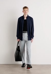 Conjunto casual que incluye una camiseta azul marino, una camiseta sin mangas negra, pantalones gris claro y zapatos negros con acentos rojos, llevando un bolso tote negro.