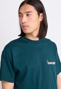 Dunkeltürkises Baumwoll-T-Shirt mit kurzen Ärmeln, rundem Kragen und kleinem gesticktem "Carhartt WP"-Logo auf der Brust.
