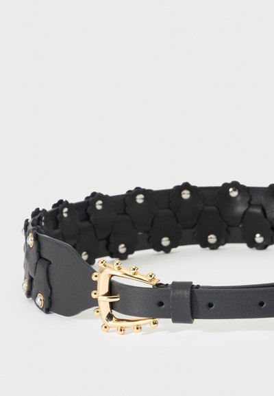 Ceinture en cuir noir avec boucle cloutée dorée et clous décoratifs noirs en forme de fleur avec petits rivets argentés.