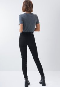 Jeans skinny de cintura alta negros con una textura suave, complementados con una camiseta de manga corta gris. Calzado incluye botas negras hasta el tobillo.