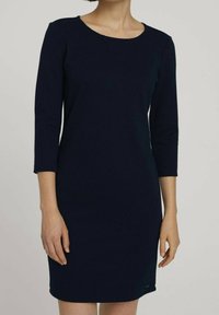 Granatowa sukienka z rękawami do 3/4, wykonana z teksturowanego materiału, z okrągłym dekoltem i dopasowanym krojem, sięgająca powyżej kolan.