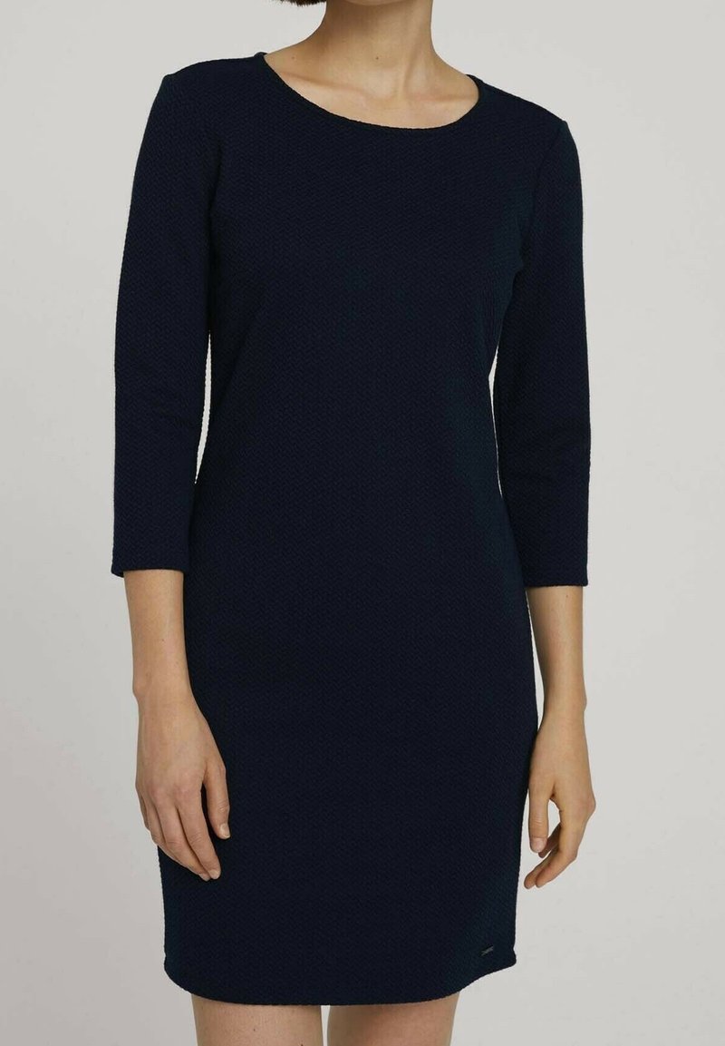 Granatowa sukienka z rękawami do 3/4, wykonana z teksturowanego materiału, z okrągłym dekoltem i dopasowanym krojem, sięgająca powyżej kolan.