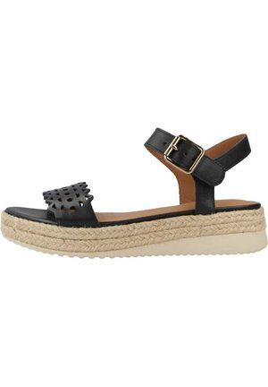 Sandalia de cuero negro con diseño de recortes, correa en el tobillo y hebilla. Suela plataforma envuelta en yute con base de goma beige.