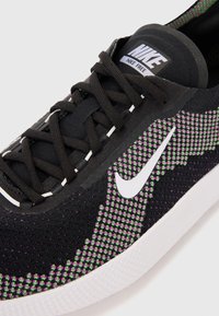 Nike Free sneakers med en overdel i sort mesh og et pixeliseret mønster i lilla og grøn, hvid swoosh og sorte snørebånd.