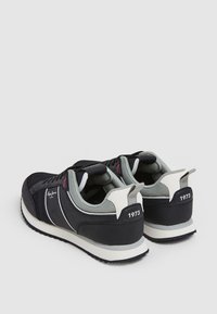 Paire de baskets noires et grises avec semelles blanches, col rembourré, et "1973" imprimé sur la languette du talon, montrées de dos et de côté.