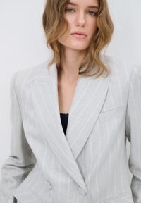 Lichtgrijs gestreept blazer met een dubbelgebreide ontwerp, gestructureerde schouders en een enkele borstzak; de stof lijkt textuur te hebben.
