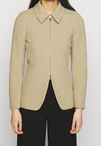 Veste beige structurée avec col chemise, fermeture éclair à l'avant et coupe ajustée, dotée de manches longues et de panneaux latéraux slim.