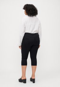 Black capri pants made of stretch fabric, featuring a mid-rise waistband, back pockets, and paired with a light long-sleeve blouse.