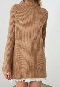 Maglione a coste beige con colletto alto indossato sopra una gonna di jeans bianca sfilacciata, mostrato dalla metà del busto a metà coscia.