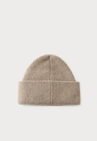 Bonnet beige en maille côtelée avec un large revers plié sur un fond clair uni.