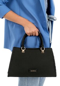 Schwarze Handtasche mit gesteppten Details, silberner Hardware und kurzen Griffen. Texturiertes Gewebe und rechteckige Form, von einer Hand gehalten.