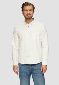 Helles kariertes Button-up-Hemd in Weiß- und Grüntönen; verfügt über einen Kragen, eine Brusttasche und lange Ärmel. Getragen mit blauen verwaschenen Jeans.