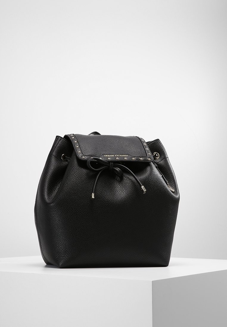 Mochila de cuero negro con una superficie texturizada, cierre de cordón y una solapa adornada con tachuelas. Presenta acentos de hardware plateado.