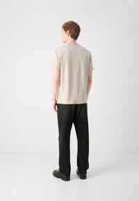 Beige kortærmet t-shirt, glat tekstur, parret med løstsiddende sorte jeans og sorte ankelstøvler, set fra ryggen.